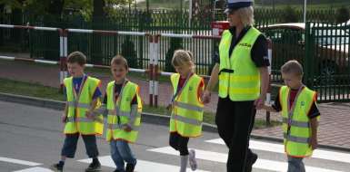 Dzieci oraz policjantka w kamizelkach odblaskowych, na pasach